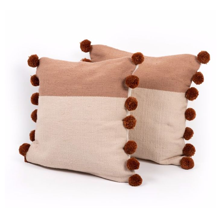 two pillows with pom - poms on them, one in beige and the other in brown