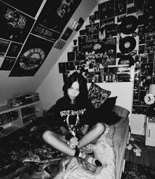 a woman sitting on top of a bed next to a wall covered in pictures and cds