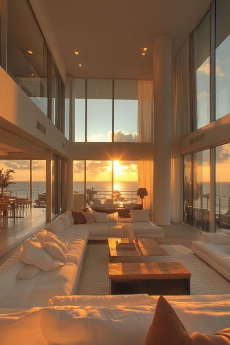 a living room filled with lots of white furniture and large windows overlooking the ocean at sunset