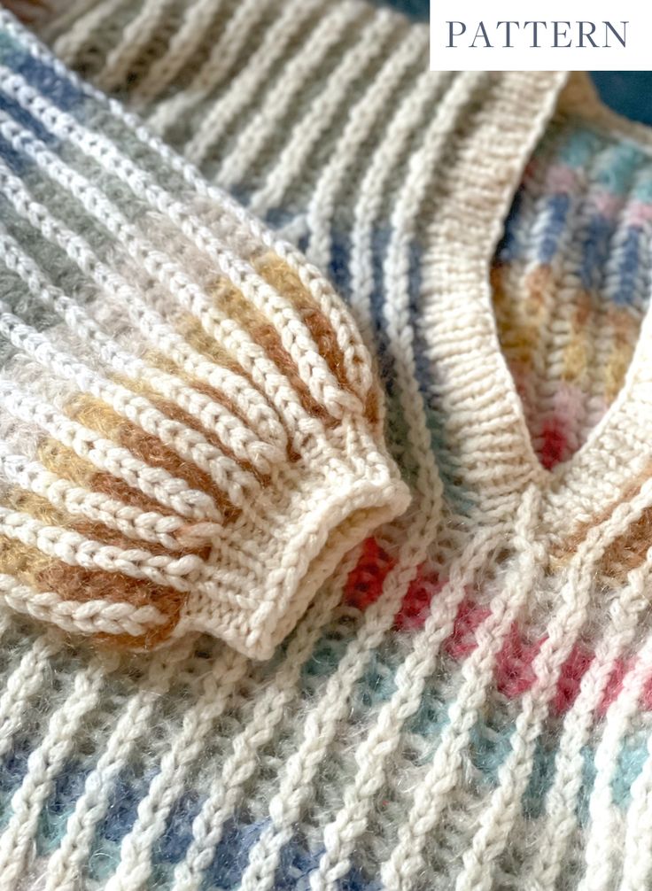 a knitted sweater sitting on top of a bed next to a blue and white blanket