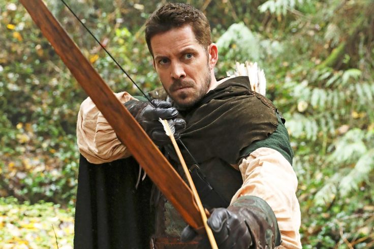 a man dressed in medieval clothing holding a bow and arrow while standing in the woods