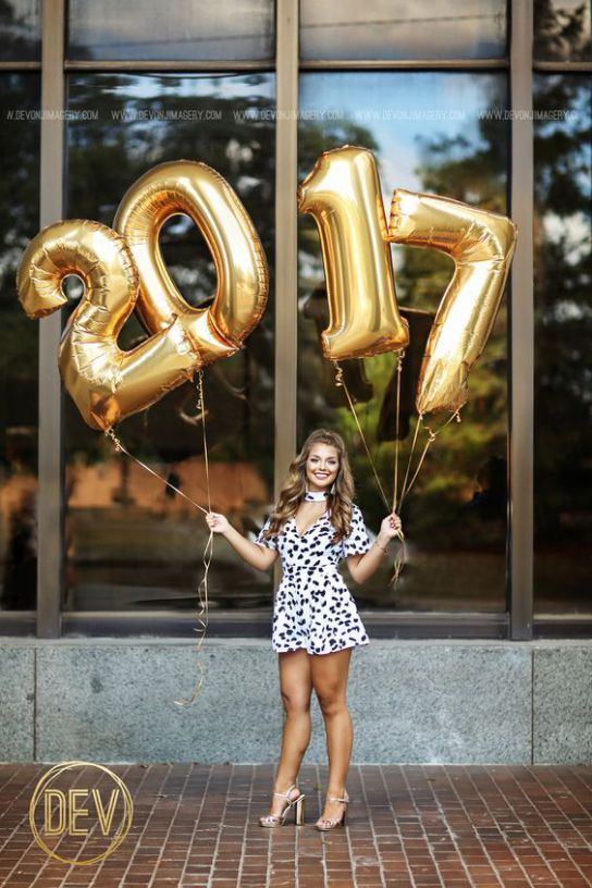 a woman standing in front of a building holding two gold balloons and the number twenty five