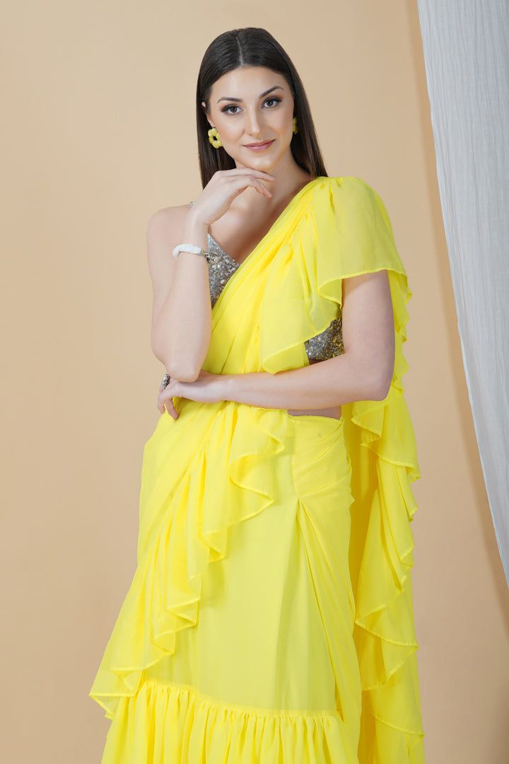 Groove at the cocktail party or a friend's wedding in this stunning frilly saree. Whimsical and lightweight, it is well paired with a contrasting strappy silver blouse that enhances the overall appeal to make it a perfect pick this season.Style Frill saree Silver embellished blouse Sunshine yellow hue Georgette fabric Specifications Model height - 5'9" Model wearing - S Festive Pre-draped Ruffled Saree, Party Saree With Cutdana And Draped Style, Party Sharara With Cutdana And Draped Design, Party Wear Draped Sharara With Cutdana, Elegant Pre-draped Saree With Ruffles For Navratri, Evening Ruffled Blouse Piece For Diwali, Diwali Evening Ruffled Blouse Piece, Evening Blouse Piece With Ruffles For Diwali, Diwali Evening Blouse Piece With Ruffles