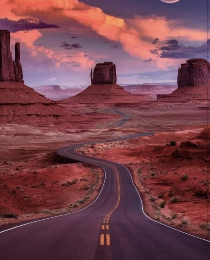 an empty road in the middle of desert with mountains and rocks behind it at sunset