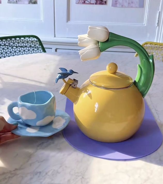 a yellow teapot with a blue cup and saucer next to it on a table