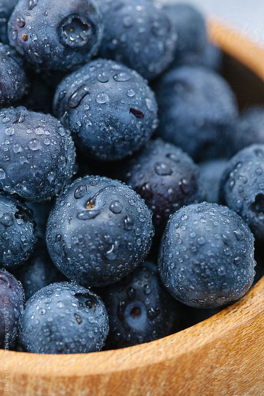 a wooden bowl filled with blueberries covered in water droplets