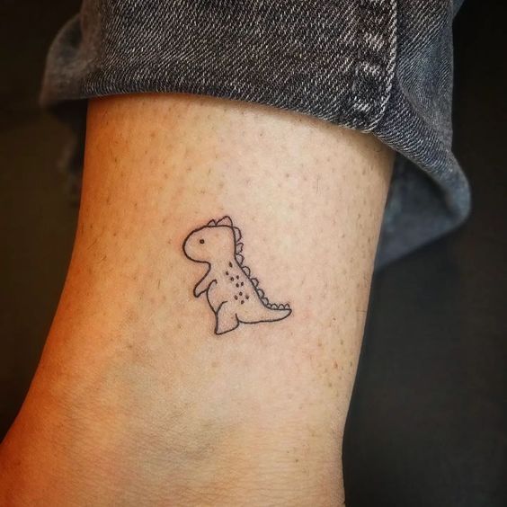 a small dinosaur tattoo on the left side of the ankle, which has a tiny outline