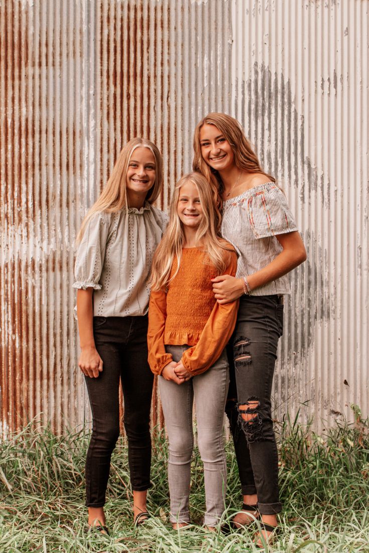 three girls standing in front of an old corrugated building with their arms around each other