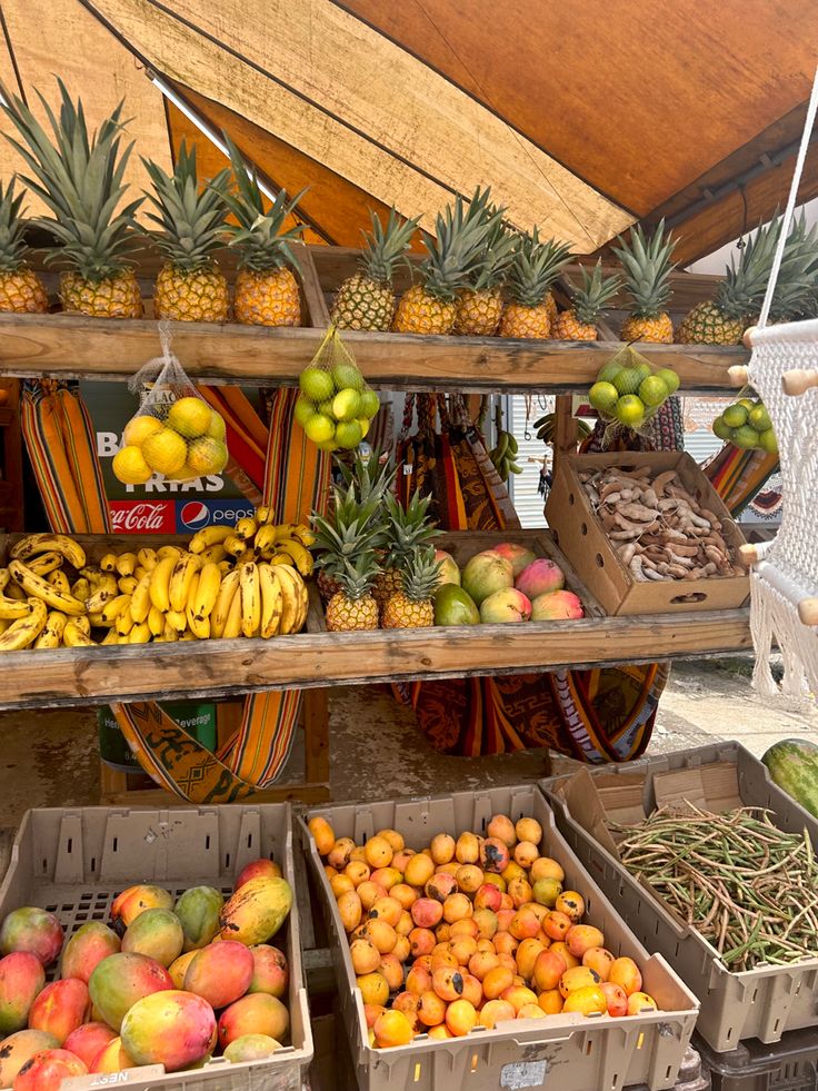 various fruits and vegetables are on display under a tent at a farmers market, including pineapples, oranges, bananas, watermelon