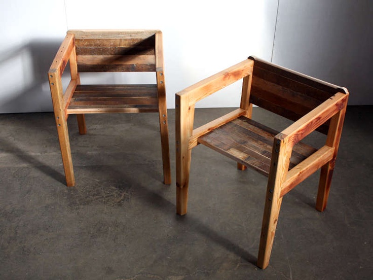 two wooden chairs sitting next to each other on top of a cement floor in front of a white wall