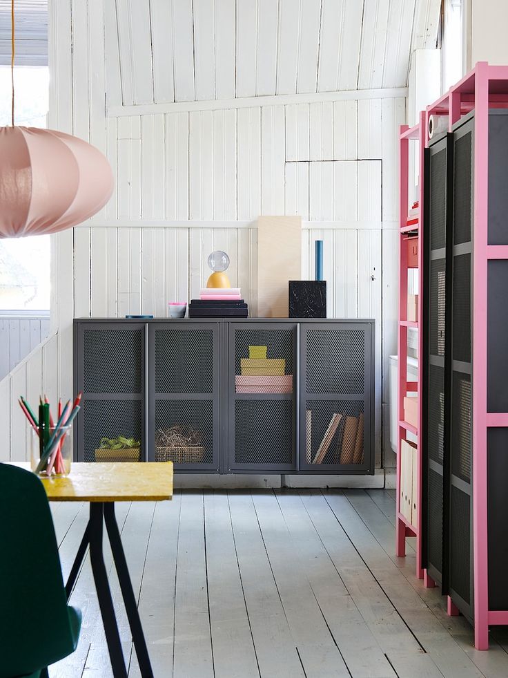 a room with white walls and wooden floors has pink shelving, green chair, and yellow table