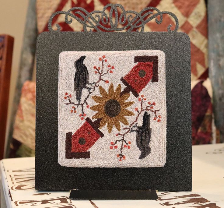 a black and white square with birds on it sitting on top of a table next to a quilt