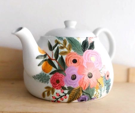 a teapot with flowers painted on it sitting on top of a wooden table next to a white wall