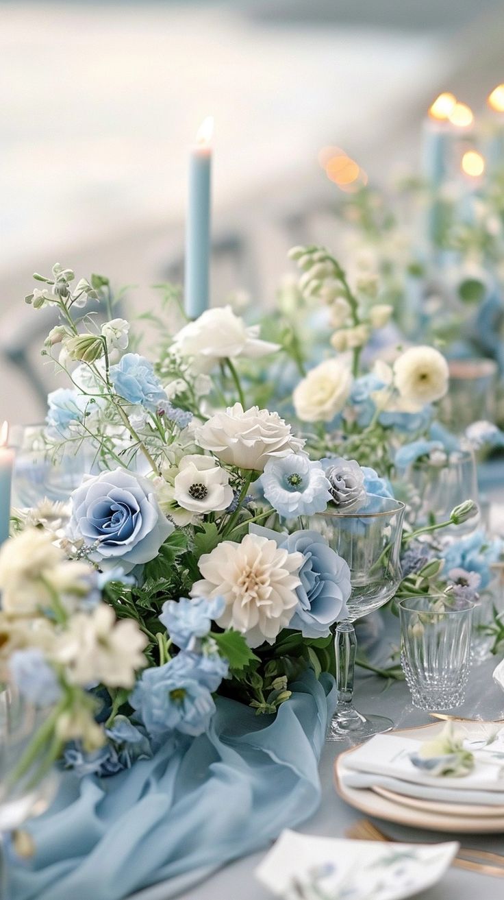 the table is set with blue and white flowers, candles and napkins on it