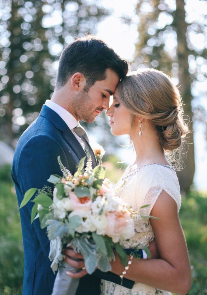 a bride and groom standing together in front of some trees with their arms around each other