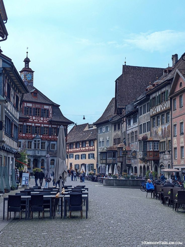 people are sitting at tables in the middle of an old town square with tall buildings