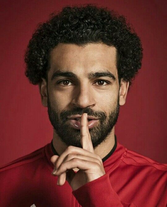 a man with curly hair and beard is posing for the camera while holding his finger to his lips