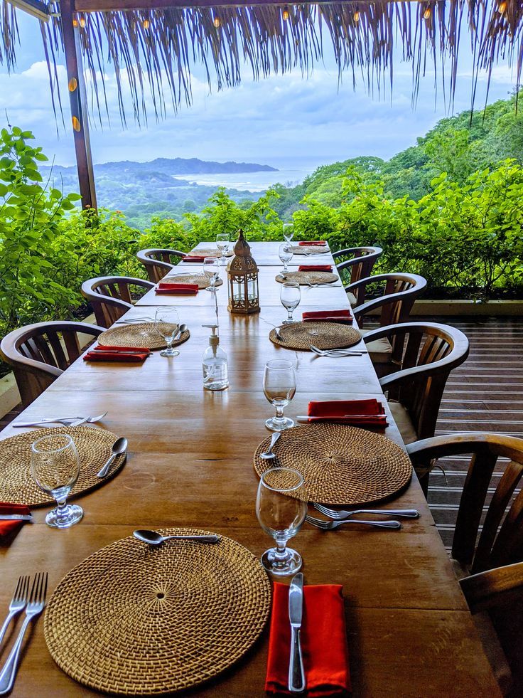 a long table with place settings on it in front of an ocean and mountains view