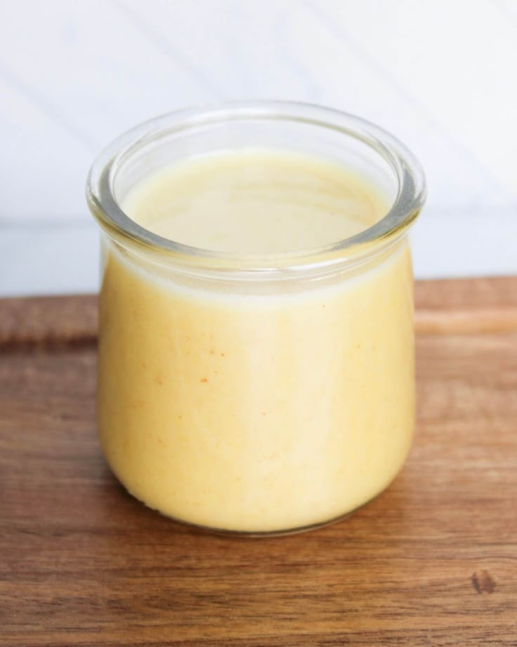 a glass jar filled with yellow liquid sitting on top of a wooden table next to a white wall