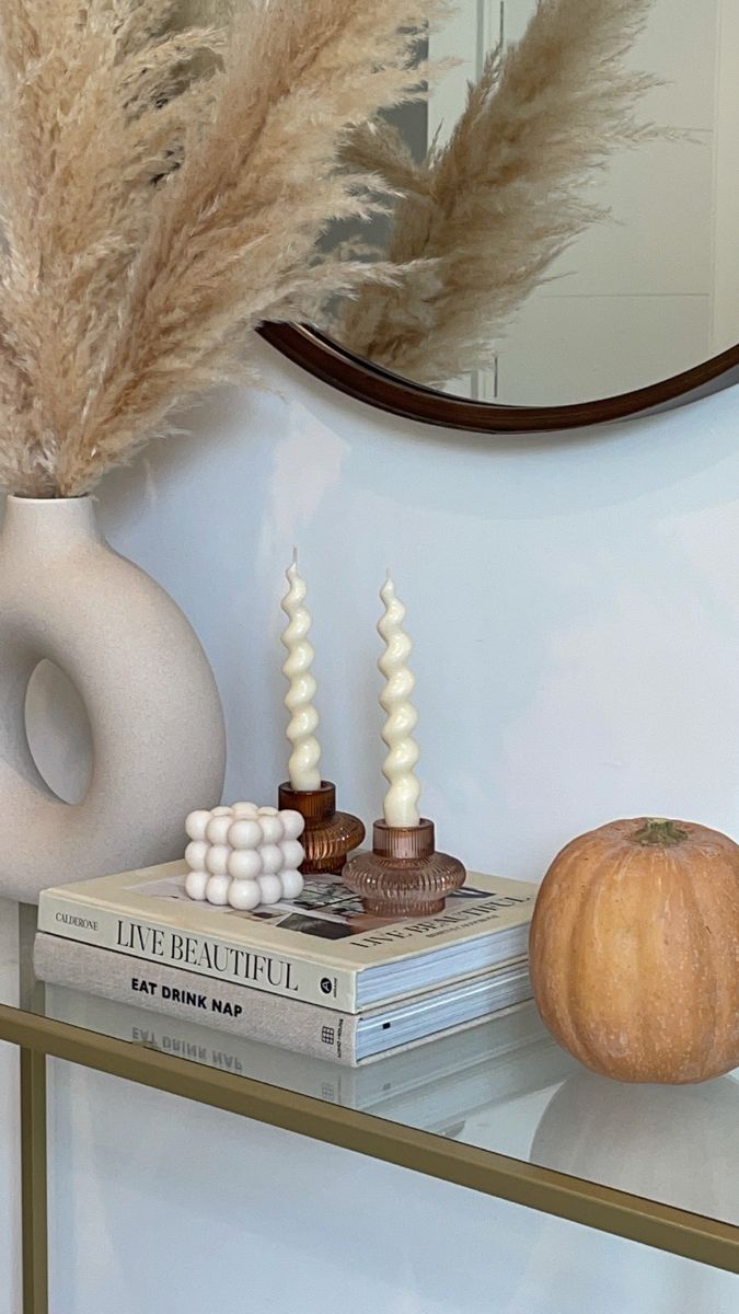 a white vase sitting on top of a table next to a stack of books and an orange pumpkin