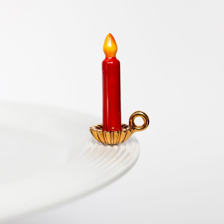 a red candle with a golden handle on a white plate, against a white background