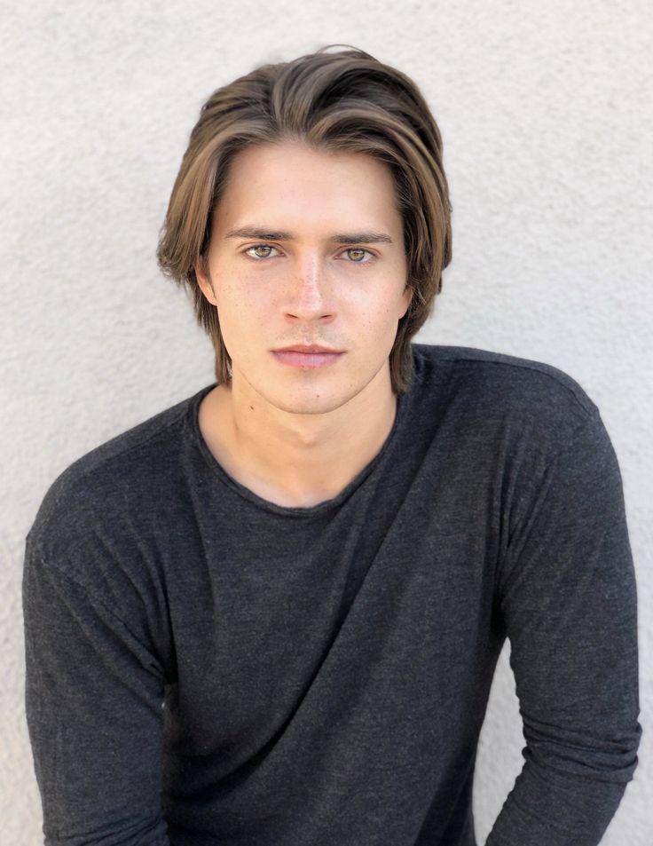 a young man with long hair is posing for a photo in front of a white wall