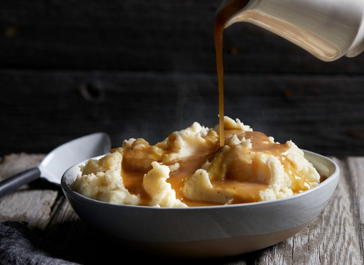 a white bowl filled with mashed potatoes and caramel sauce being poured on top