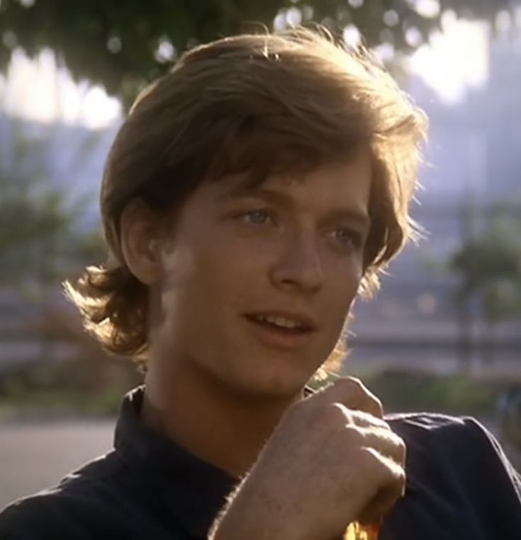 a young man with long hair wearing a polo shirt and holding his hand on his shoulder