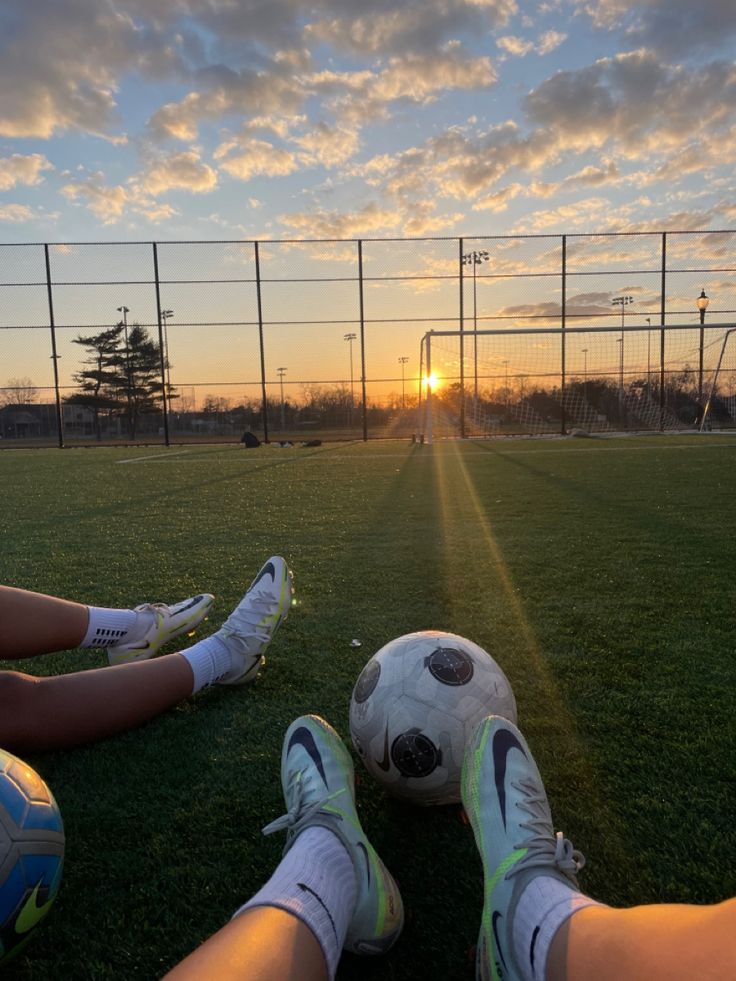 two soccer players are sitting on the grass with their feet propped up in front of a soccer ball