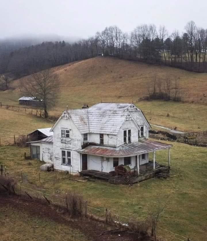 an old white house sitting on top of a lush green field next to a hill