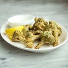 a white plate topped with broccoli and lemon wedges next to a bowl of ranch dressing