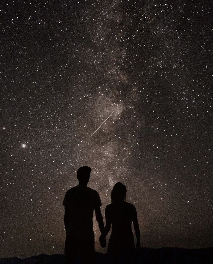 two people standing under the stars in the night sky