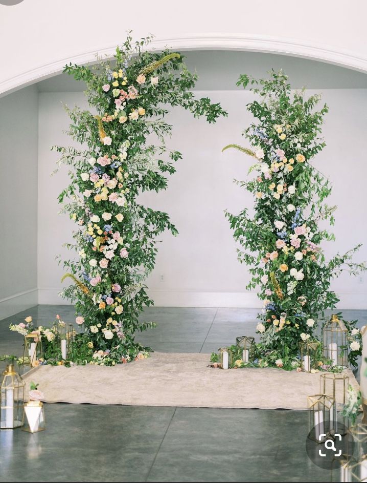 an arch covered in flowers and greenery with candles on the floor next to it