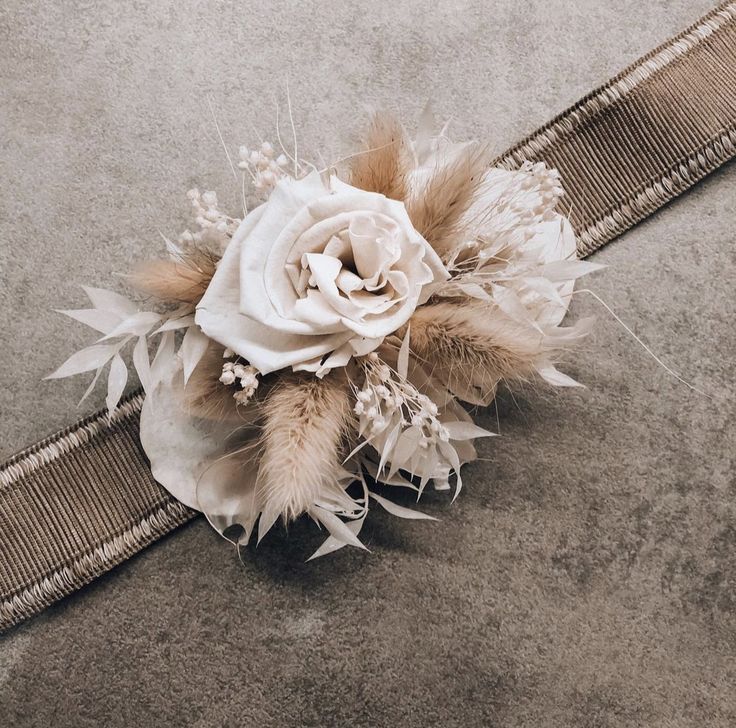 a white rose and feathers corsage on the ground next to a metal belt