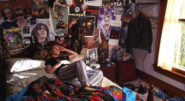 a woman laying on top of a bed in a bedroom next to a wall full of posters