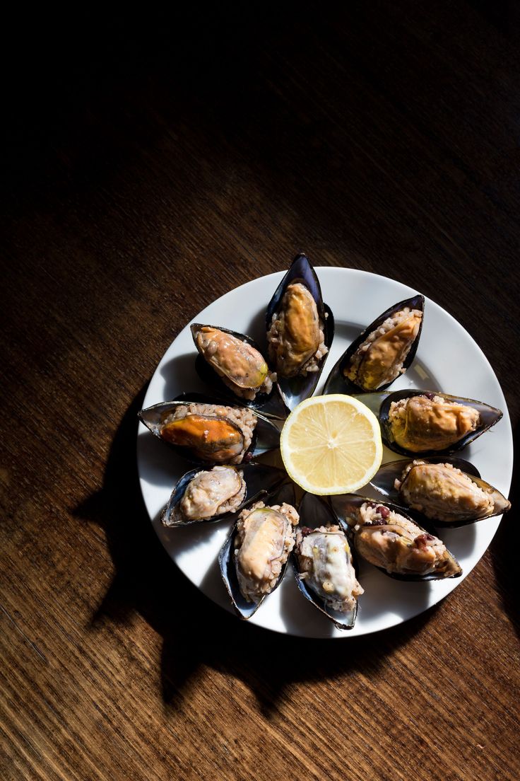 a white plate topped with mussels next to a slice of lemon on top of a wooden table