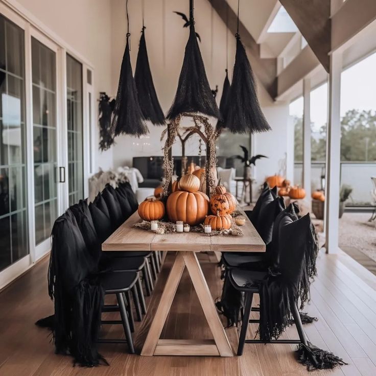 a wooden table topped with black chairs and pumpkins