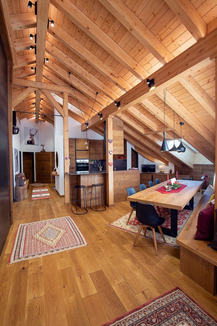 an open living room and kitchen area with wood flooring, exposed beams and wooden ceiling