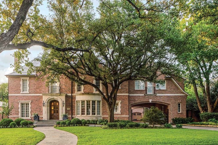 a large brick house with trees in the front yard and walkway leading up to it