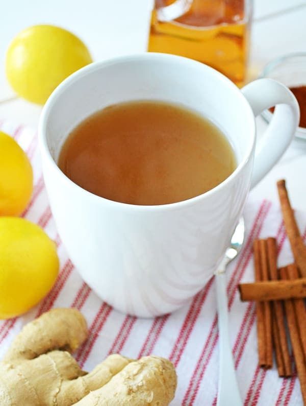 a cup of ginger tea next to some lemons and cinnamon sticks