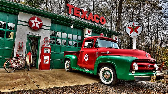 an old red and green truck parked in front of a texaco gas station