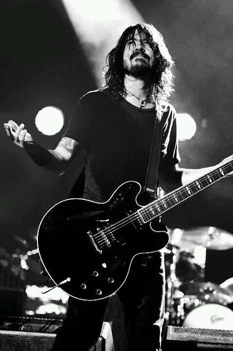 a black and white photo of a man with long hair playing an electric guitar on stage