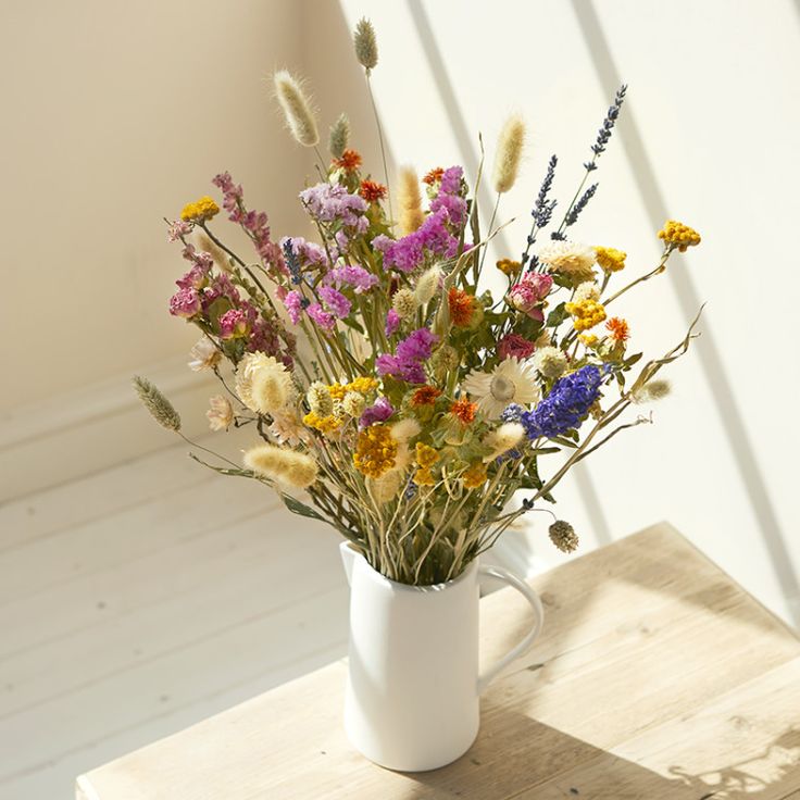 a bouquet of wildflowers in a white vase sitting on a wooden table next to a window