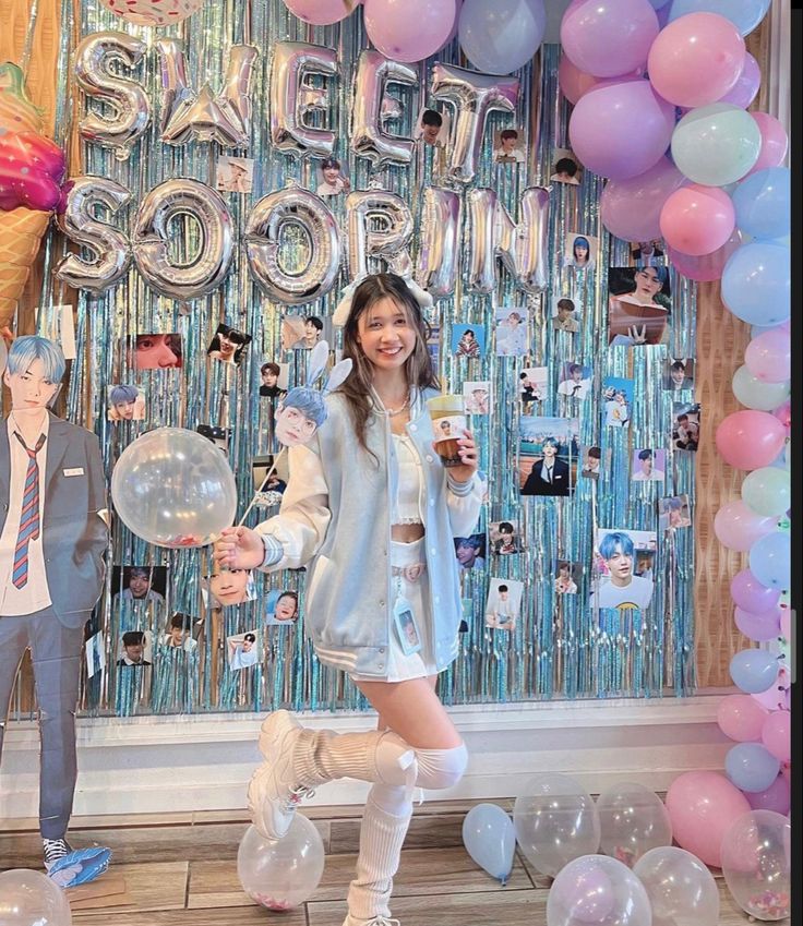 two people standing in front of balloons and streamers with one person holding a drink