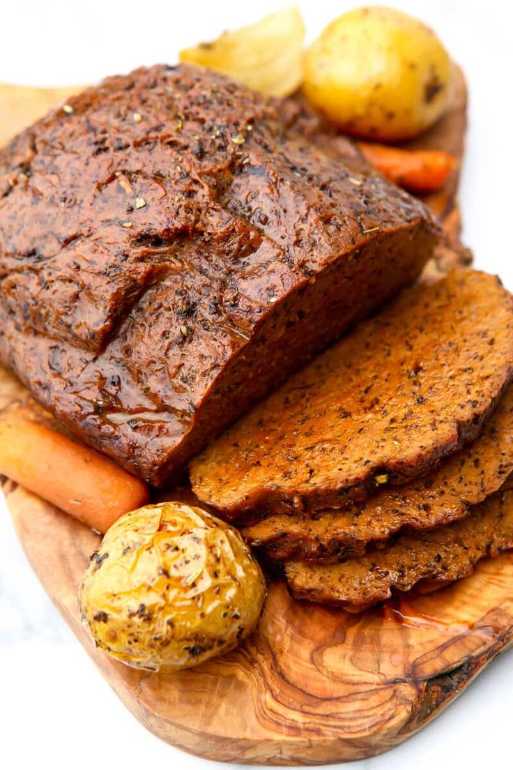 a wooden platter with meat and vegetables on it, including carrots and potatoes