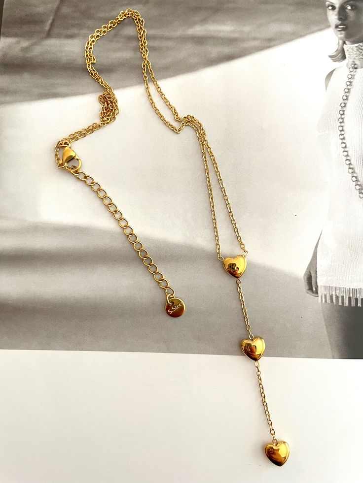 Rehaussez votre look avec ce collier lariat triple cœur. Fabriqué de manière experte en acier inoxydable et fini avec un placage or, il ajoute une touche de luxe moderne à n'importe quel ensemble. Avec trois cœurs, c'est le moyen idéal d'exprimer votre style et votre amour. Three Hearts, Triple Heart, Elevate Your Look, Lariat Necklace, Touch Of Modern, Modern Luxury, Gold Plating, Your Style, Gold Plate