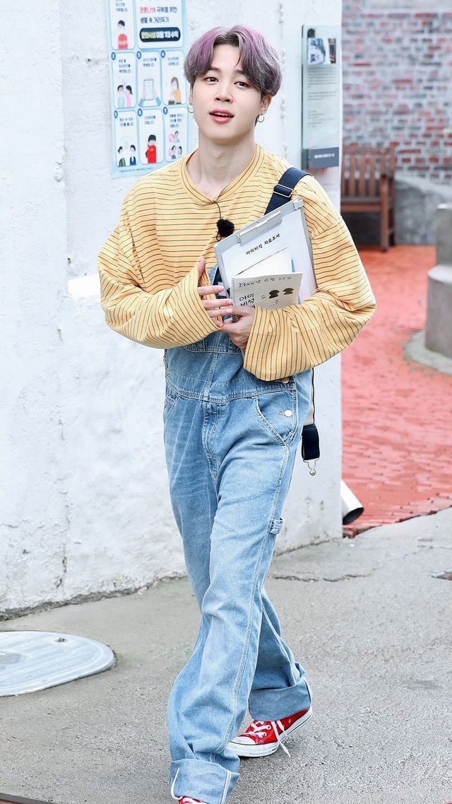 a young boy with pink hair is walking down the street wearing blue jeans and a yellow sweater