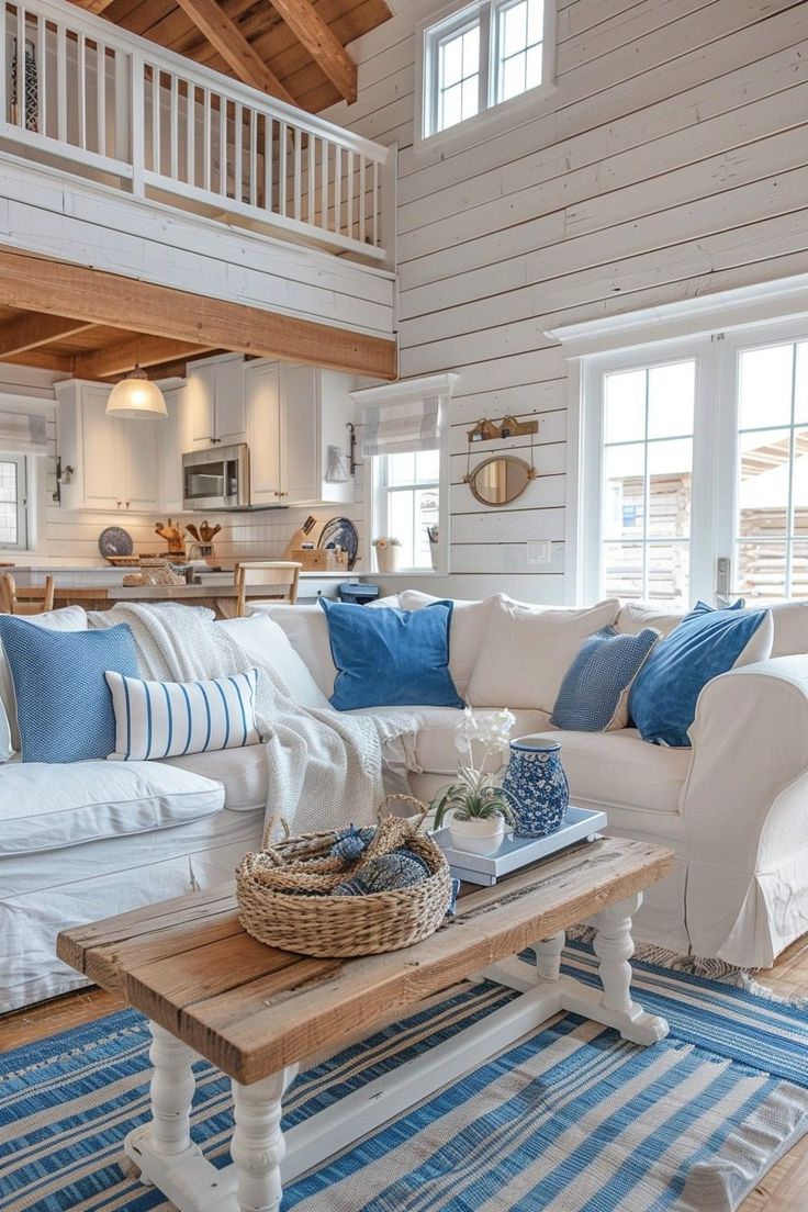 a living room filled with white furniture and blue pillows on top of a wooden table