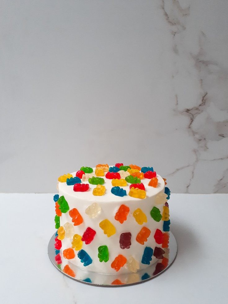 a multicolored cake with white frosting and gummy bears on the top