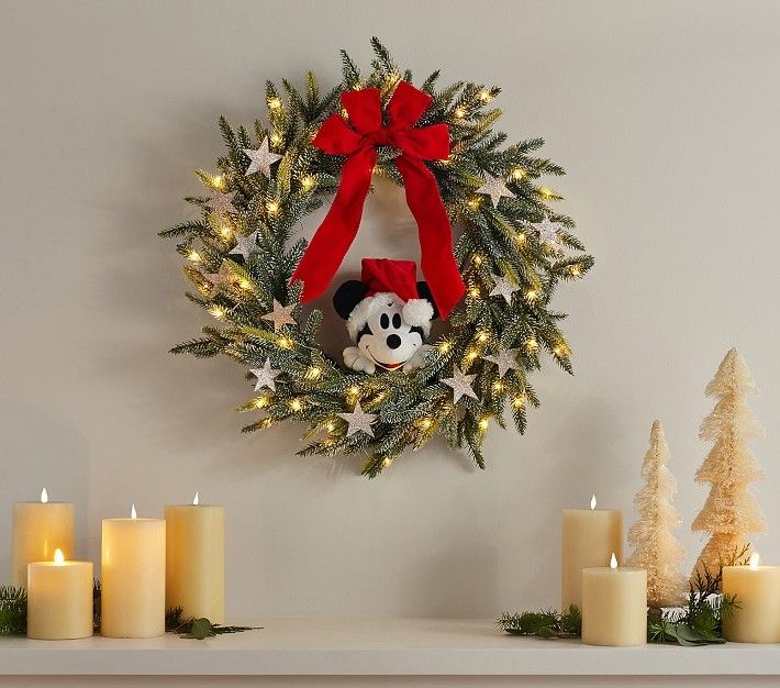 a christmas wreath with a mickey mouse head hanging on the wall next to lit candles